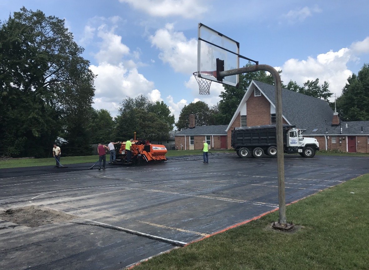Crew paving an outdoor basketball court with fresh asphalt