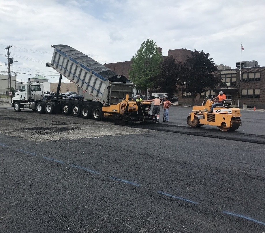 Tri-Axle dump truck feeding asphalt paver with roller and crew on an industrial repaving project
