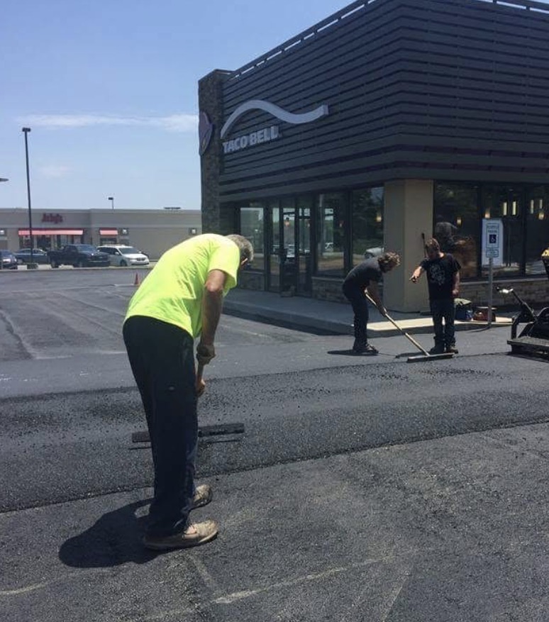 Paving crew hand-raking fresh asphalt at a Taco Bell parking lot