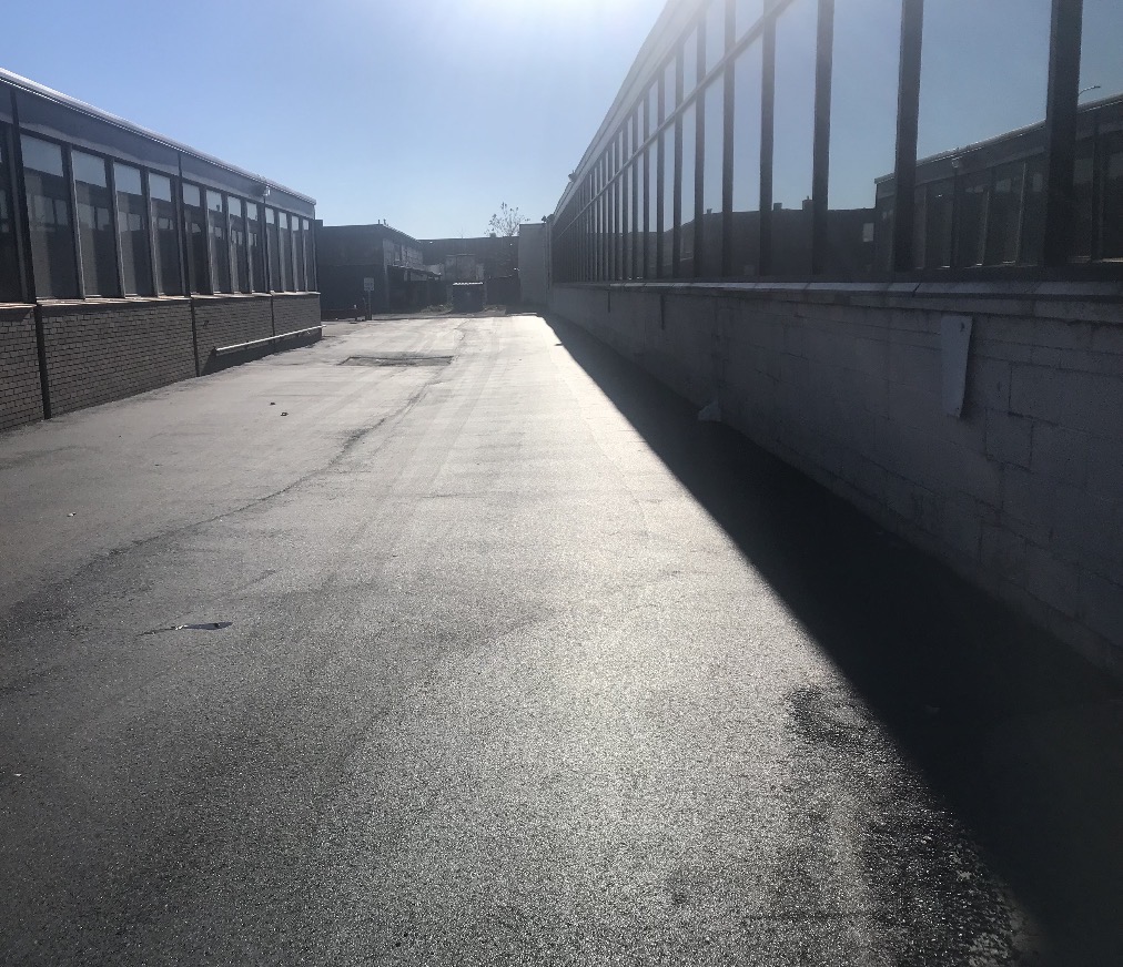 Freshly paved asphalt alley between brick industrial buildings
