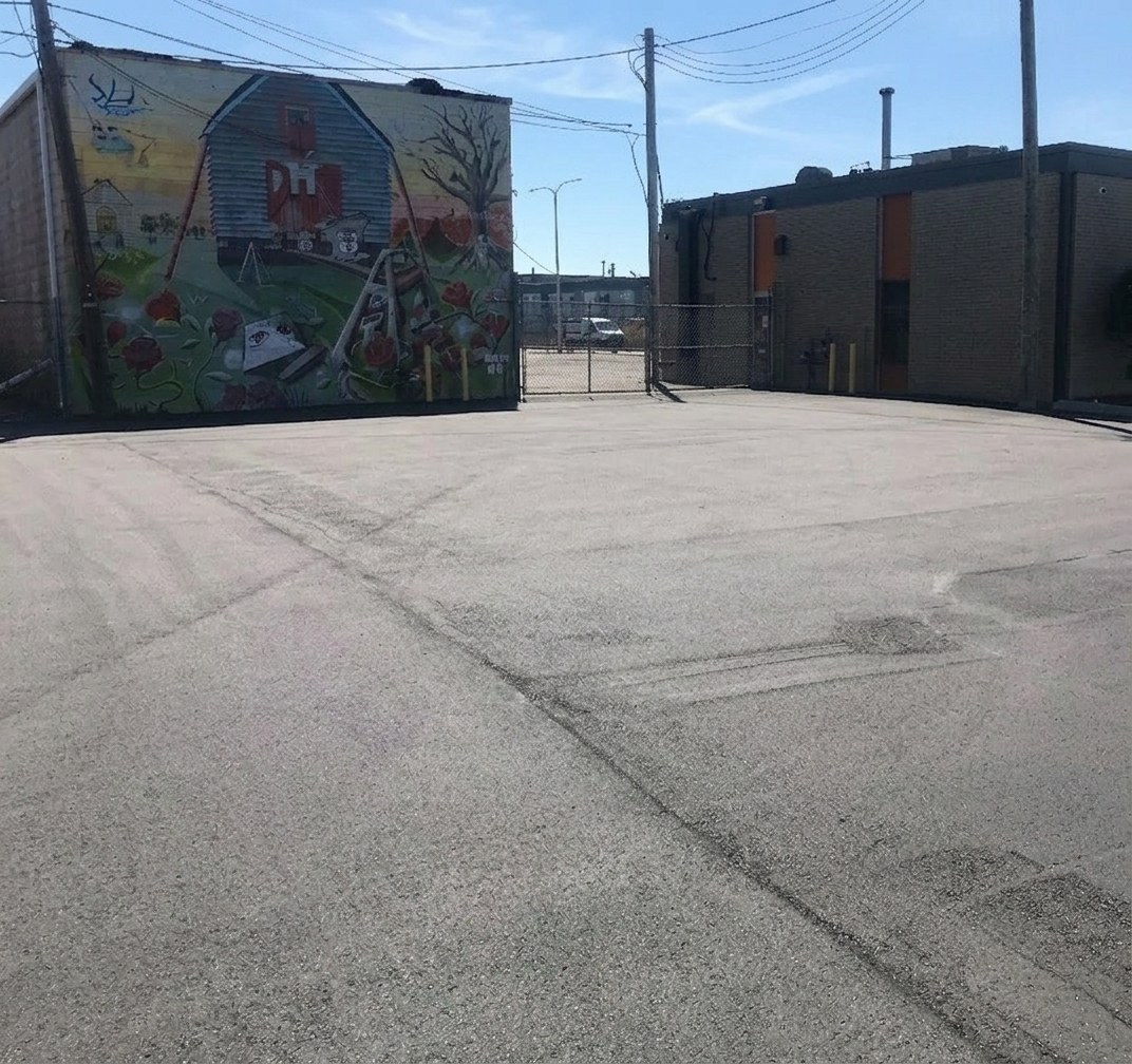 Freshly paved industrial parking lot beside a building with a large mural