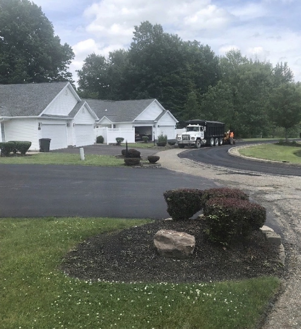 Paving crew with dump truck laying fresh asphalt driveways at a residential townhouse community